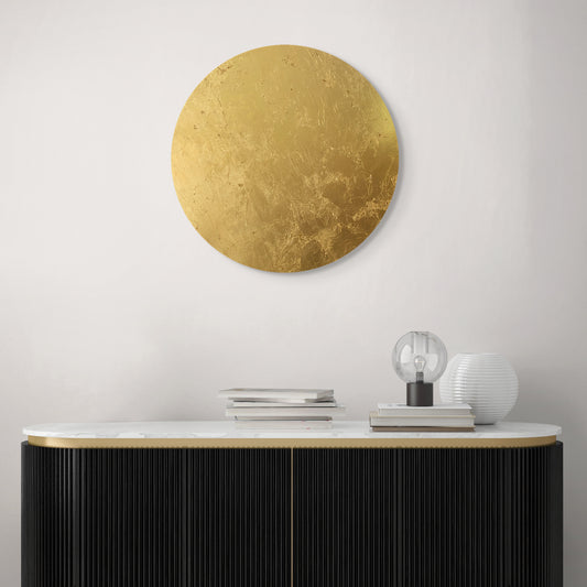 A gold leaf applied to a wooden round art piece, displayed on a wall above a modern console table.