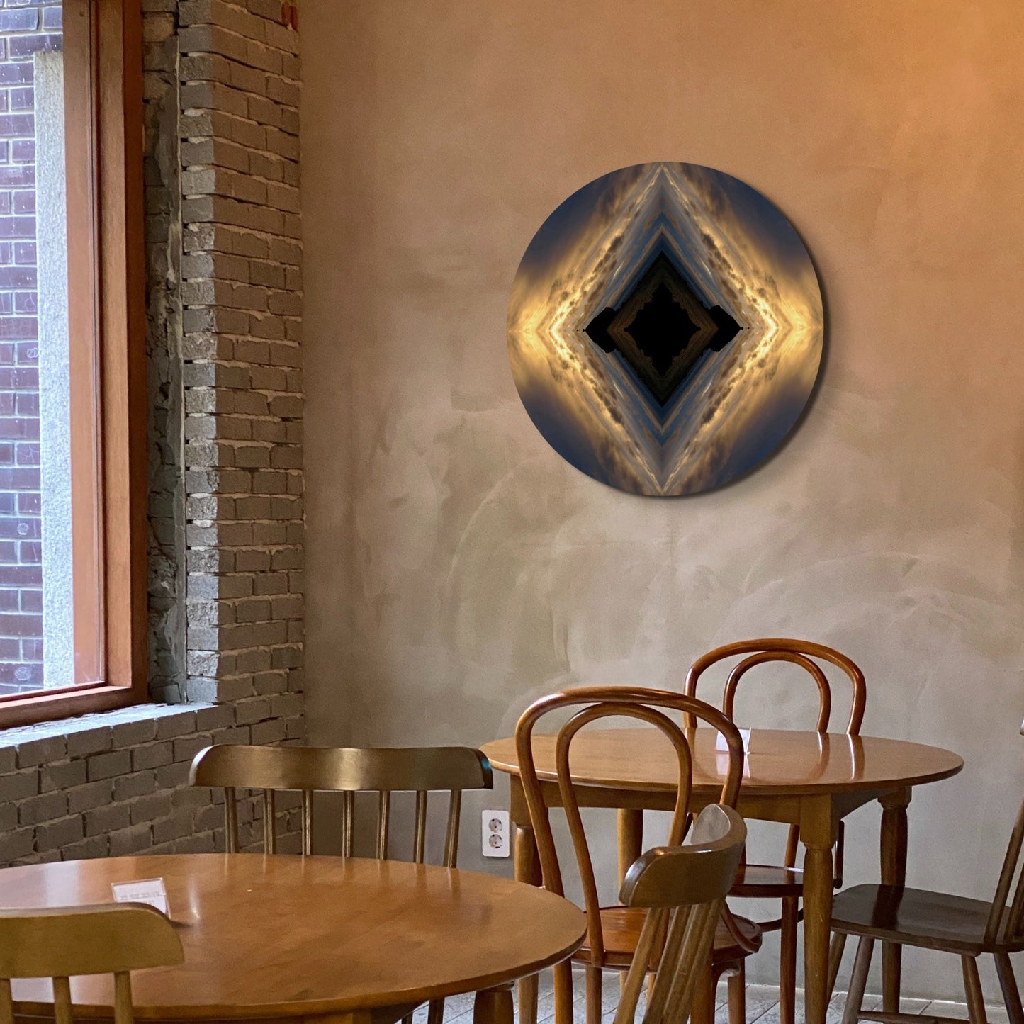 A round abstract photography print titled 'Golden Bay', displayed on a wall above wooden tables and chairs in a cafe setting.