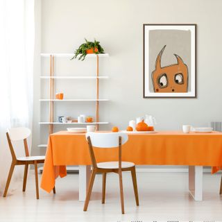 Dining room with orange tablecloth, white chairs, and a shelf with decorative items.