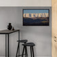 Framed mountain landscape art on a gray wall above black stools and a table.